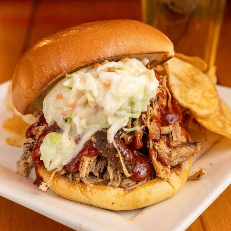 Pulled pork sandwich topped with slaw, with house chips